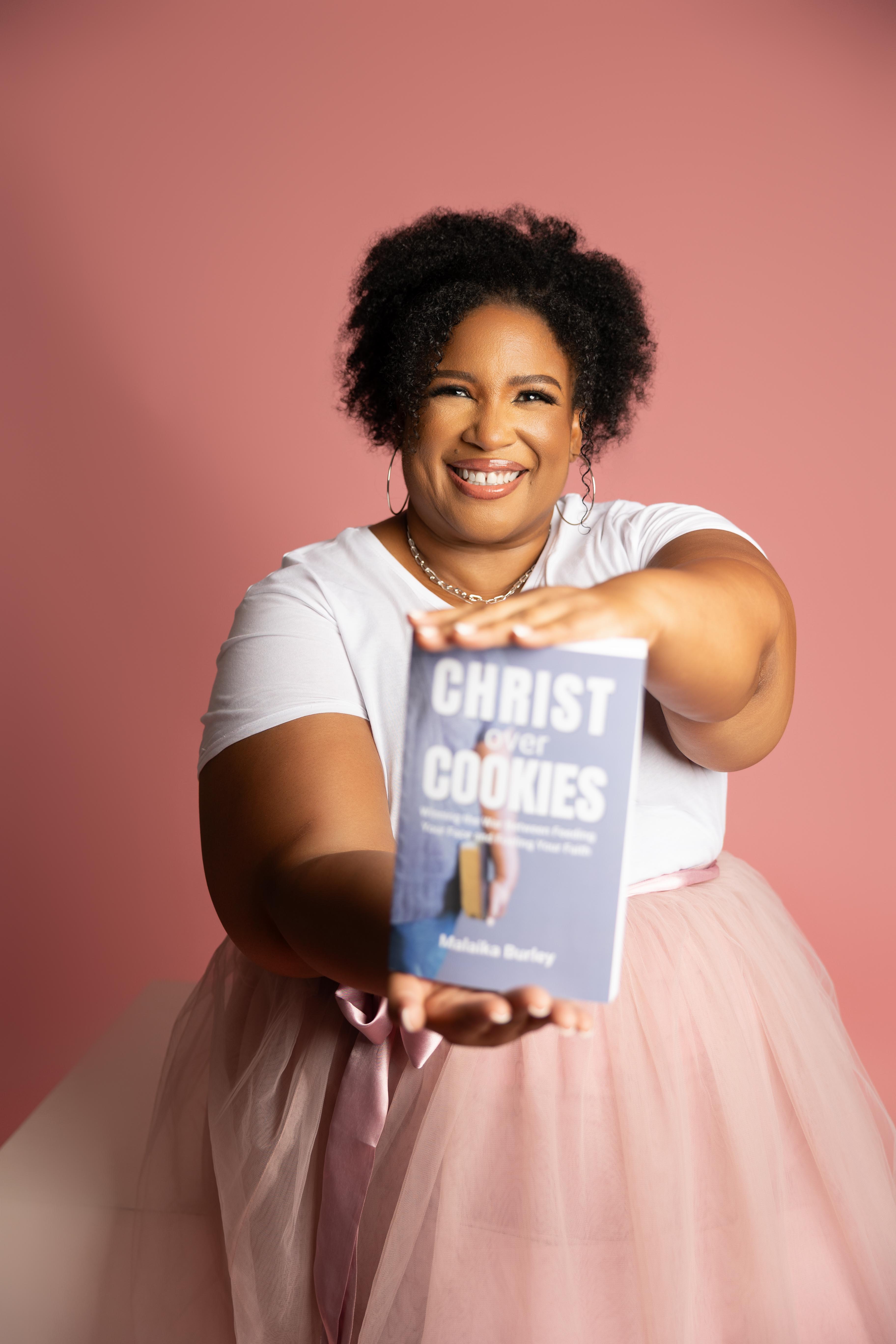 Woman holding a book titled 'Christ Over Cookies' against a pink background